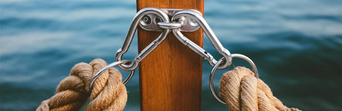 Two lengths of rope held by metal hooks on a wooden post, with blue water behind